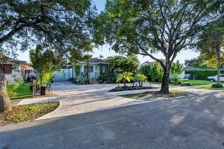 Exterior featuring a concrete driveway, mature canopy trees, lush tropical landscaping, and a raised front entryway