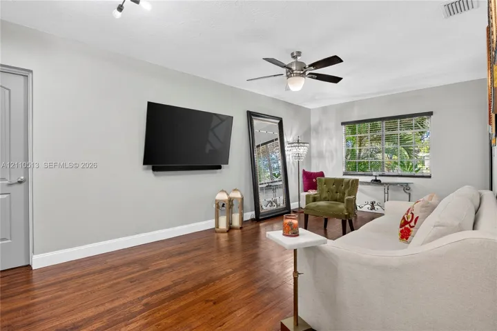 Living area featuring wood-finish flooring, a multi-blade ceiling fan with integrated light fixture, a paneled door, and a horizontal window with grid detail