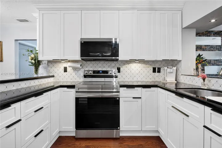 Kitchen featuring white shaker-style cabinetry, stainless steel appliances, dark stone countertops, decorative tile backsplash, and wood-finish flooring