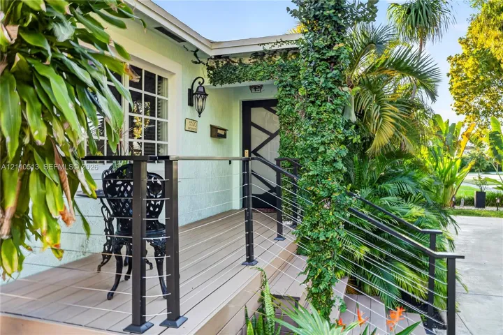 Elevated porch featuring composite decking, black metal cable railings, custom geometric front door, and traditional wall-mounted lantern lighting