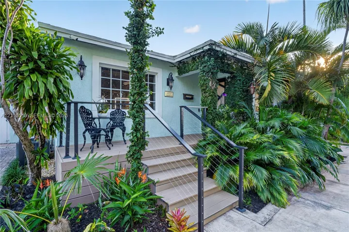 Exterior featuring light-colored stucco siding, raised composite decking, metal cable railings, and established landscaping