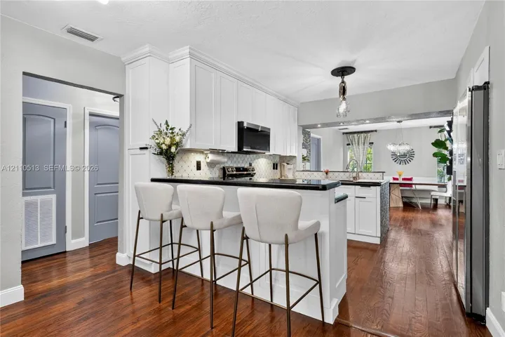 Kitchen featuring white shaker-style cabinetry, dark stone countertops, wood-finish flooring, a breakfast bar, and a decorative tile backsplash
