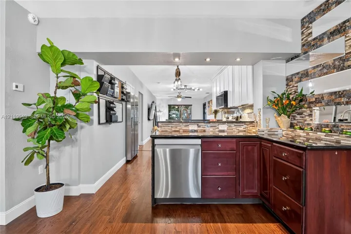 Kitchen featuring dark wood cabinetry, stainless steel dishwasher, stone-tile backsplash, dark countertops, and wood-finish flooring