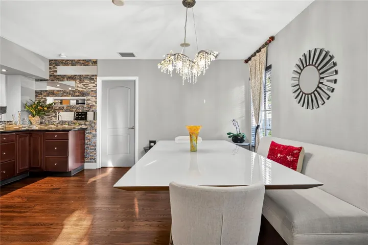 Dining area featuring wood-finish flooring, a tiered crystal chandelier, an intricate stacked-stone accent wall, and cabinetry with dark-toned finishes