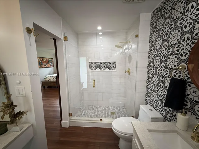 Walk-in shower featuring a glass enclosure, brass-finish fixtures, a decorative tile niche, and penny-round tile flooring, complemented by a patterned tile accent wall and stone-surfaced vanity