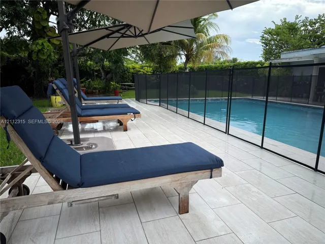 In-ground swimming pool featuring a removable mesh safety fence and light-toned tile pool deck surrounded by mature landscaping