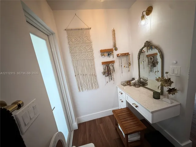 Floating vanity featuring a solid surface countertop, soft-close drawers, wall-mounted brass light fixture, and wood-finish flooring