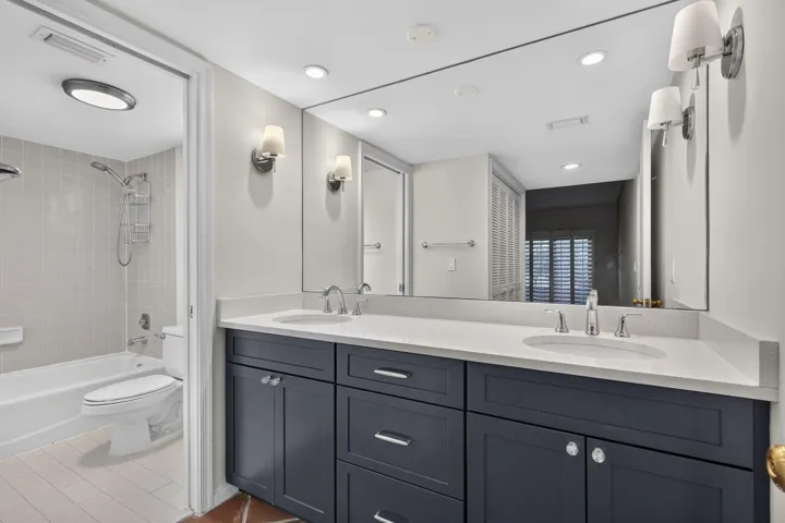 Dual-sink vanity with a solid-surface countertop, dark-toned cabinetry, recessed lighting, wall-mounted light fixtures, and a tiled shower-tub combination