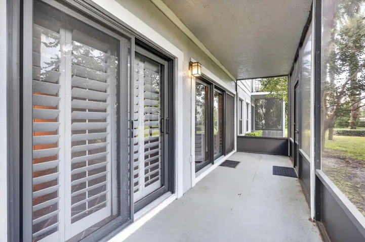 Screened-in porch featuring concrete flooring, dark metal framing, sliding glass doors with white plantation shutters, and a wall-mounted exterior light fixture