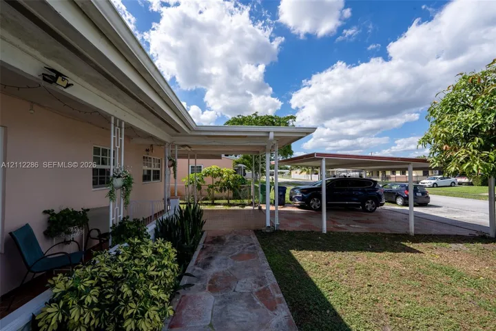 Covered entryway featuring decorative structural columns, stone-paver walkway, and attached carport