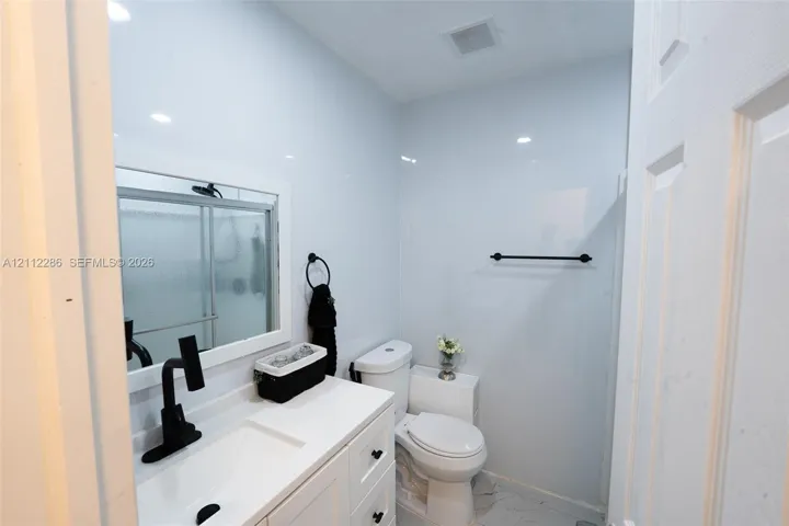 Bathroom featuring a white vanity cabinet with an integrated sink, matte black faucet, framed mirror, and tile wall surfacing