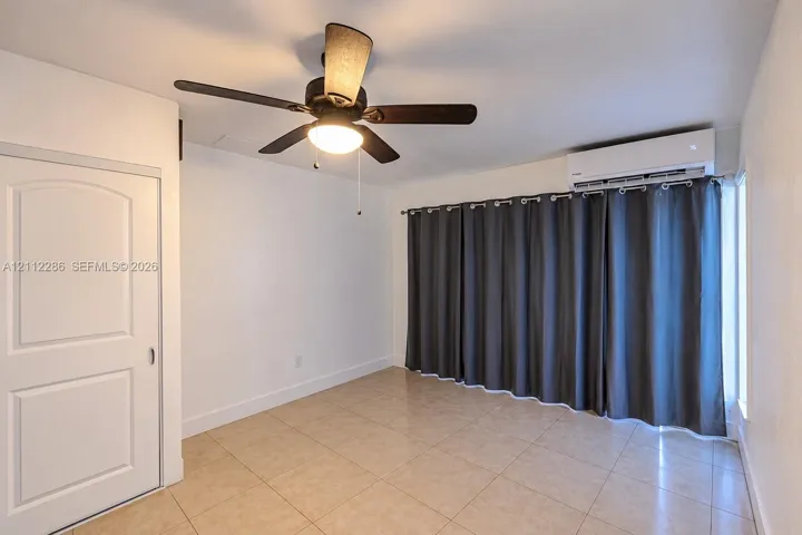 Interior space featuring neutral tile flooring, a wall-mounted ductless mini-split air conditioning unit, and a ceiling fan with integrated lighting