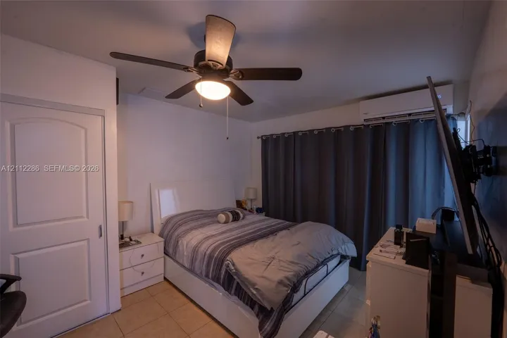 Room featuring tile flooring, a wall-mounted climate control unit, and a ceiling fan with integrated lighting