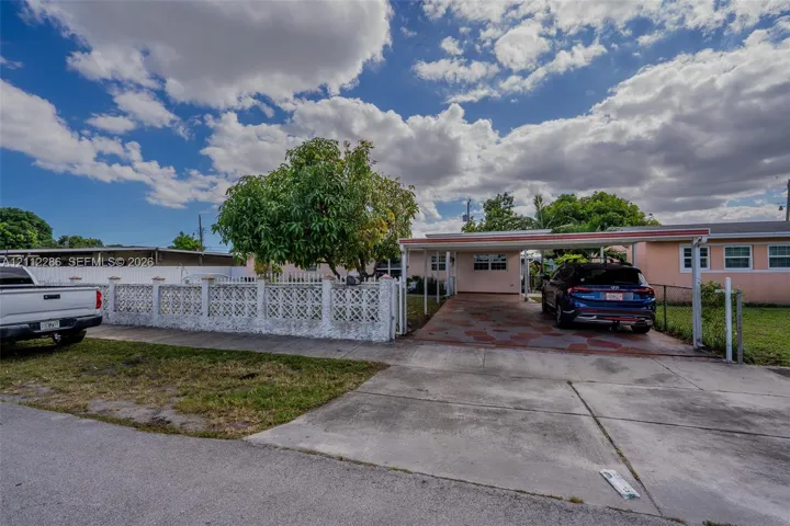 Exterior featuring a covered carport, decorative breeze block fencing, paved driveway, and mature landscaping