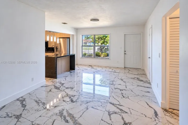 Polished stone-look flooring, kitchen island with dark solid-surface countertop, and recessed ceiling lighting