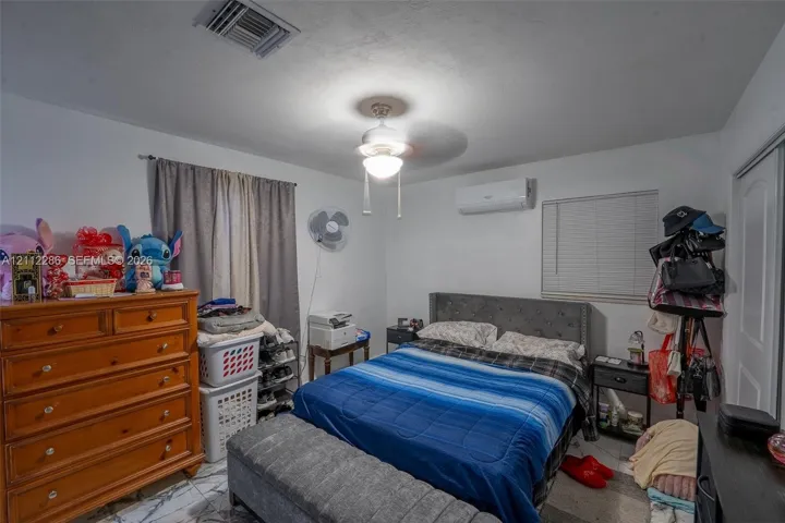 Room featuring stone-finish flooring, a wall-mounted ductless air conditioning unit, a central ceiling fan with an integrated light fixture, and horizontal window blinds