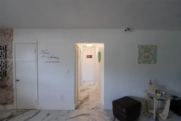 Interior space featuring white-veined stone-finish flooring, an arched entryway, louvered-door closet, and overhead flush-mount lighting
