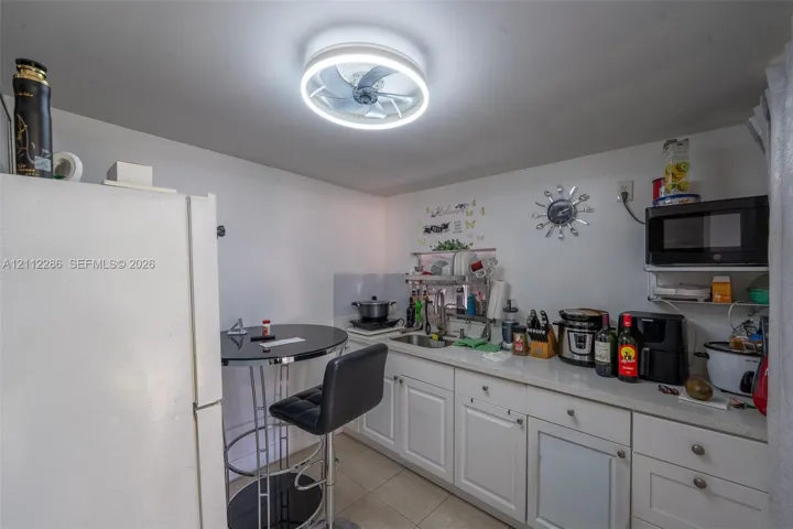 White cabinetry, integrated stainless steel sink, solid-surface countertop, and circular LED ceiling fixture