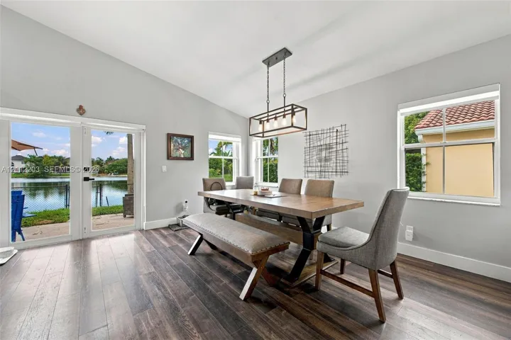 Vaulted ceiling room with wood-finish flooring, linear metal pendant lighting, and glass-paneled double doors providing water frontage