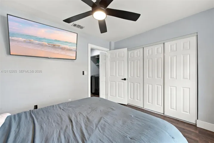 Neutral-toned interior featuring wood-finish flooring, a contemporary matte black ceiling fan with integrated lighting, and white six-panel closet doors with matching matte black hardware