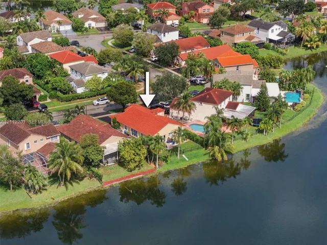 Waterfront property featuring a red tile roof, concrete driveway, and established tropical landscaping