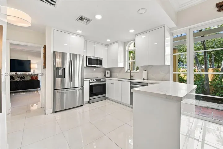 Kitchen featuring high-gloss white cabinetry, stone-finish countertops, stainless steel appliances, large-format tile flooring, and floor-to-ceiling glass paneling