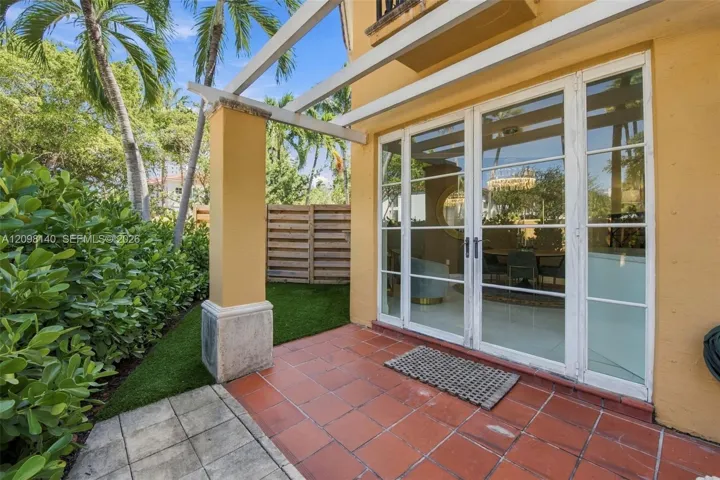 Rear patio featuring terracotta tile flooring, a white structural pergola, synthetic turf, and full-height glass French doors with white mullions