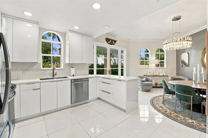 Modern kitchen featuring high-gloss white cabinetry, polished stone countertops, stainless steel appliances, arched windows, and large-format tile flooring
