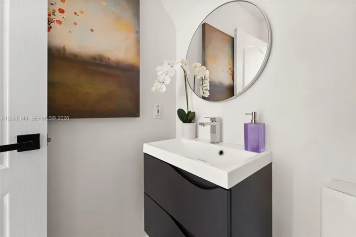 Modern wall-mounted dark cabinetry with a white integrated sink, polished chrome single-handle faucet, and circular frameless mirror