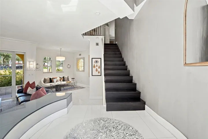 Open floor plan featuring large-format tile flooring, a dark-finish staircase, arched windows, and glass sliding doors