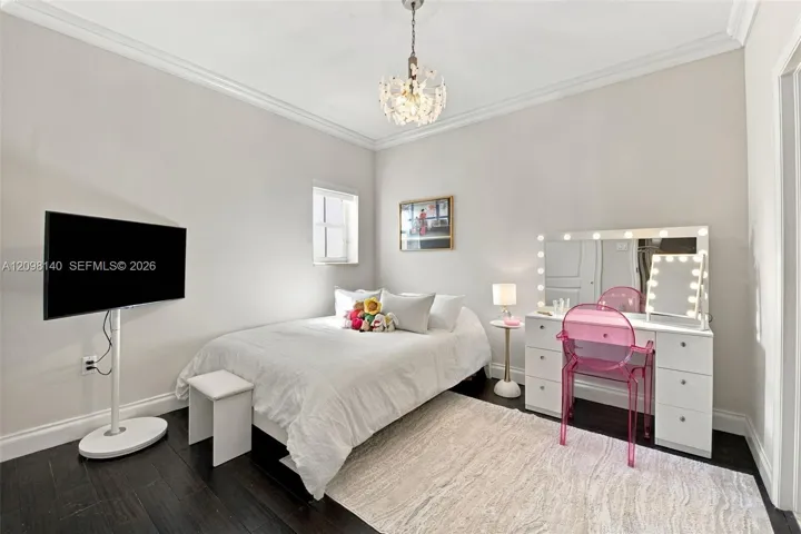 Neutral-toned bedroom featuring dark wood-finish flooring, crown molding, and a tiered crystal chandelier