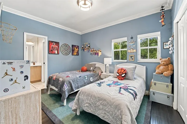Bedroom featuring dark wood-finish flooring, crown molding, double-hung windows with exterior mullions, and an attached en-suite bathroom with a built-in vanity