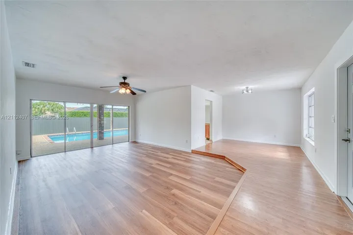 Living area featuring wood-finish flooring, a tiered floor elevation, ceiling fan, and sliding glass doors with direct exterior access to an in-ground pool