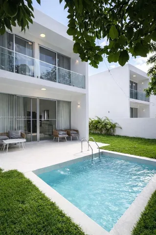 Modern architectural exterior featuring a private swimming pool, concrete patio, second-story balcony with glass railing, and floor-to-ceiling sliding glass doors