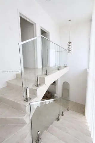 Staircase featuring stone treads, frameless glass balustrades with brushed metal hardware, and a multi-globe pendant light fixture
