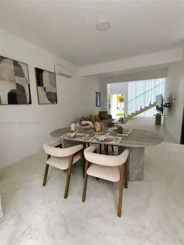 Neutral-toned interior featuring stone-finish flooring, a wall-mounted climate control unit, and an open staircase with a glass railing