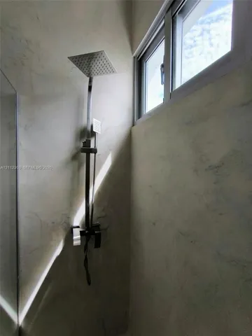 Walk-in shower featuring a rainfall showerhead, handheld spray attachment, sleek metallic hardware, and neutral wall tiling with a high-positioned horizontal window
