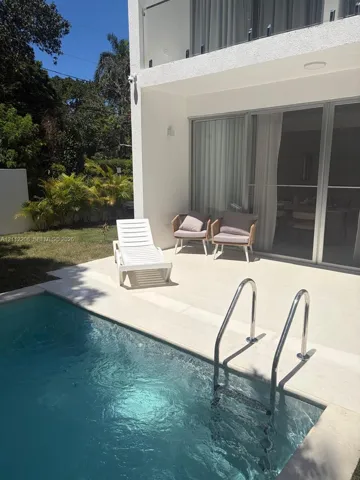 Private swimming pool with metal handrails, light-colored patio, sliding glass doors, and a glass-paneled balcony
