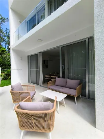 Covered terrace featuring light-toned flooring, sliding glass door entry, and a second-story balcony with a frameless glass railing