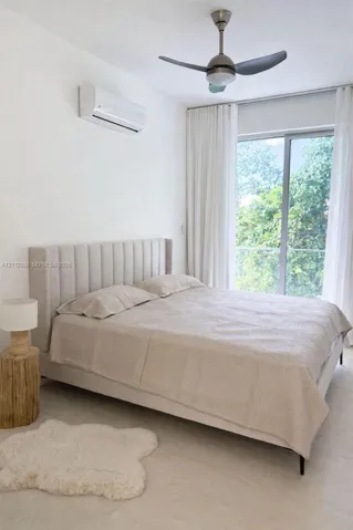 Floor-to-ceiling sliding glass door, wall-mounted air conditioning unit, neutral tone flooring, and a modern three-blade ceiling fan with integrated lighting