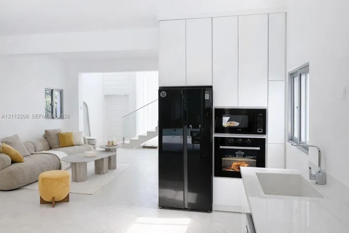 Floor-to-ceiling cabinetry, built-in wall oven and microwave, stone-surface countertop with integrated sink, and matte finish floor tile