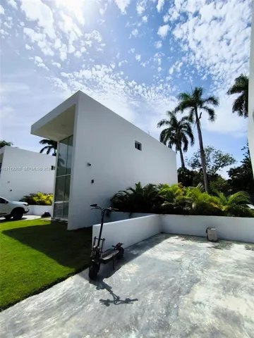 Minimalist modern exterior featuring a smooth white stucco facade, expansive floor-to-ceiling glass windows, a concrete driveway, and low-profile hardscaped perimeter walls