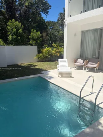 Private swimming pool with stainless steel ladder, light-colored patio decking, exterior stucco walls, and enclosed perimeter privacy wall