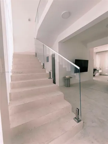 Staircase featuring light-toned stone treads and a frameless glass railing with metallic hardware
