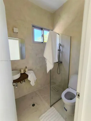 Bathroom featuring a walk-in shower with a glass partition, wall-mounted vessel sink, wood-finish floating vanity counter, wall-mounted faucet, and window with natural light