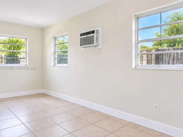 Neutral-toned interior space featuring light-colored ceramic tile flooring, three multi-pane windows, and a wall-mounted air conditioning unit