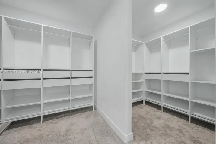 Walk-in closet featuring white built-in shelving, integrated hanging rods, multiple storage drawers, and neutral carpeting