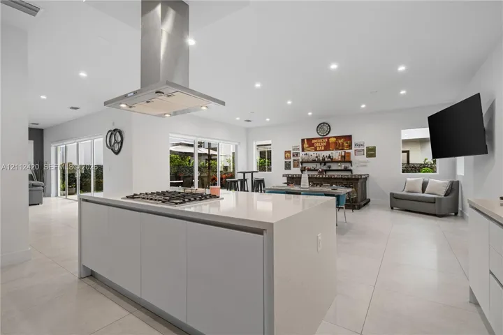 Kitchen featuring a large central island with quartz countertops, built-in gas cooktop, stainless steel ventilation hood, and light-colored tile flooring