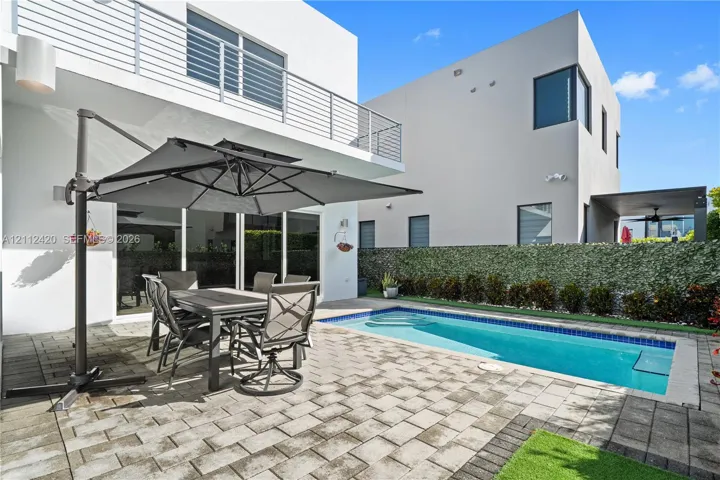 Modern exterior featuring a paved stone patio, in-ground swimming pool, horizontal metal balcony railing, and floor-to-ceiling sliding glass doors