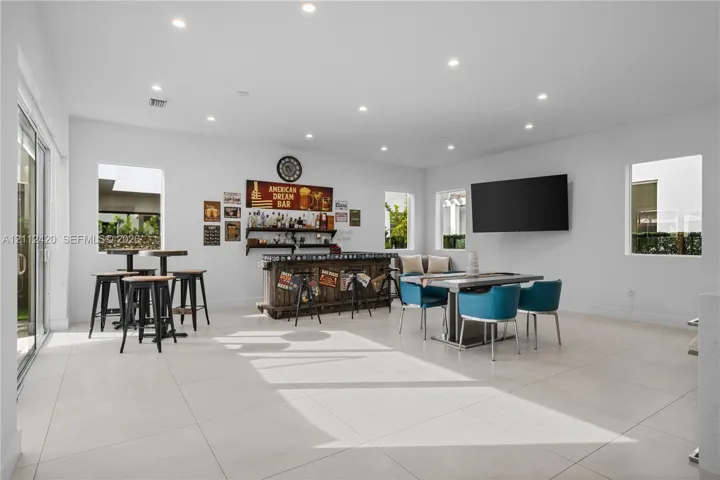 Spacious room featuring large-format tile flooring, recessed lighting, and a built-in bar area with wood cabinetry